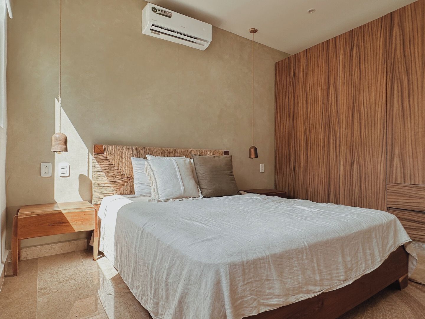 Une chambre à coucher comprenant un lit, des tables de chevet, un appareil de climatisation et une armoire en bois.