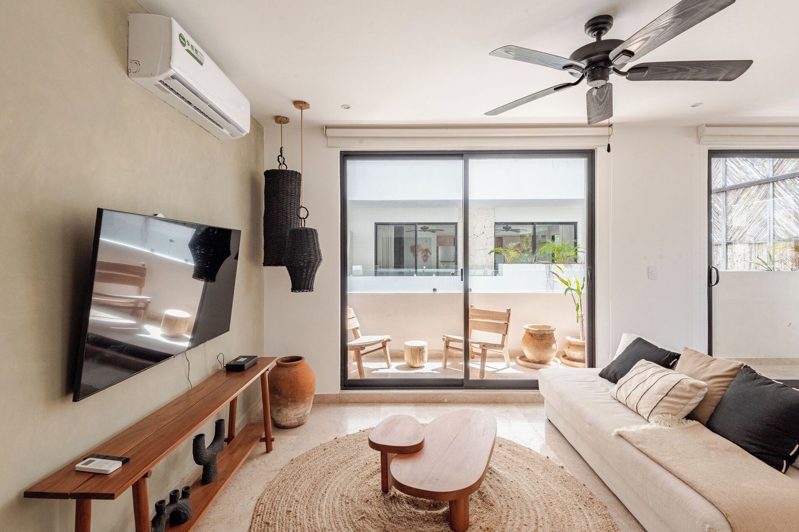 A modern living room with a flat-screen TV, a ceiling fan, a sofa, and a dining area with a table and chairs.