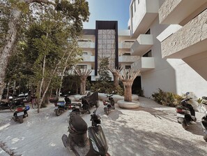 A courtyard with multiple motorcycles parked, surrounded by trees and a building with a modern design. - Aldea Zama · 2BR with pool · Guest favorite (Tulum)