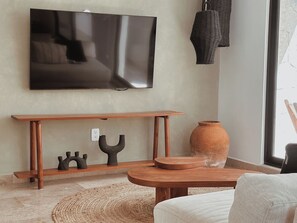 A living room with a flat-screen TV mounted on the wall, a wooden coffee table, a round rug, and a large terracotta pot. - Aldea Zama · 2BR with pool · Guest favorite (Tulum)