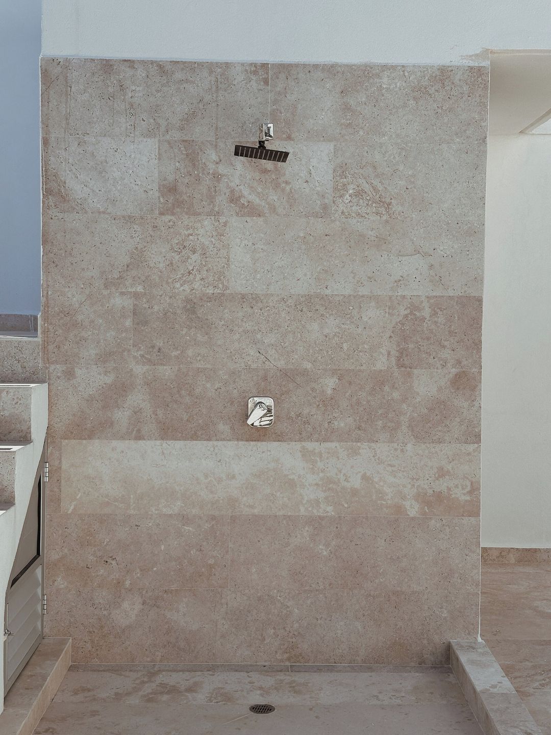 A shower enclosure with a tiled wall, a drain, and a control panel.