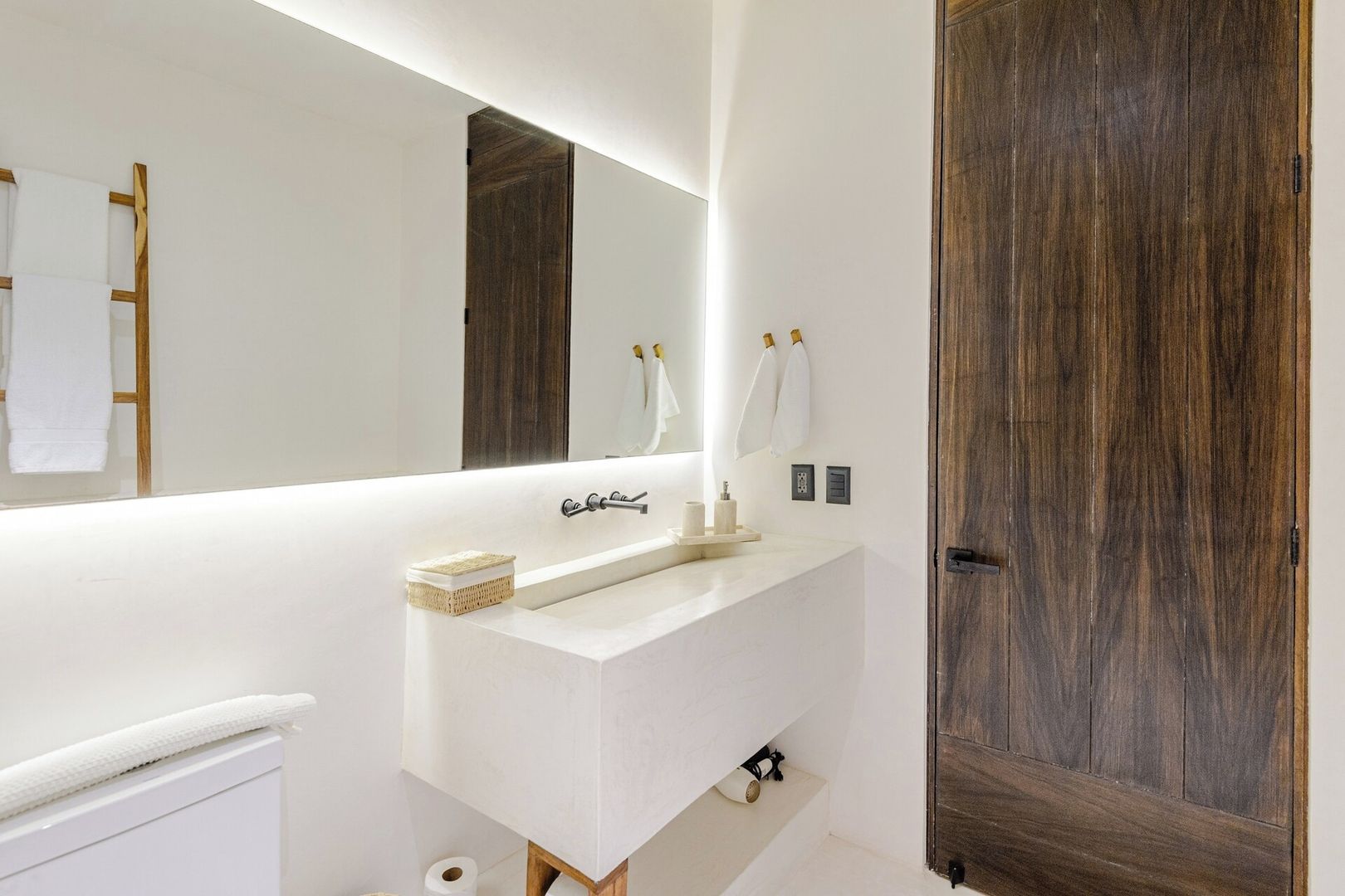 A bathroom with a white vanity, a large mirror, a wooden door, and a towel rack.