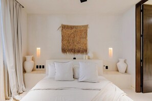 A bedroom with a large bed, two bedside tables, a woven wall hanging, and a wooden door. - La Veleta · Exclusive private pool · 1BR couple (Tulum)