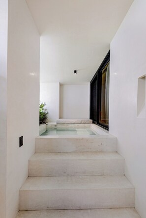 Eine Treppe führt zu einem Poolbereich mit minimalistischem Design, weißen Wänden und einer Glaseinfriedung.