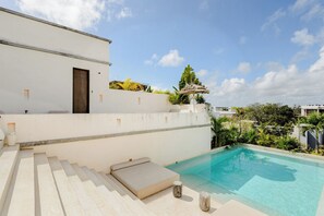 Ein moderner Poolbereich im Freien mit einem klaren, blauen Pool, einer Liege und einer Treppe, die zu einem weißen Gebäude mit einer Tür führt.