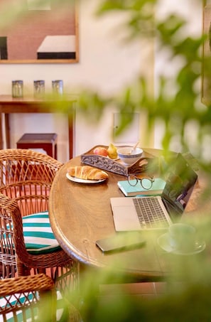 Ein runder Holztisch mit einem Laptop, einer Brille, einer Schüssel mit einem Löffel, einem Teller mit einem Croissant und einem Buch.