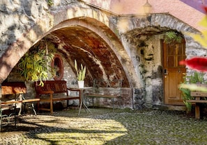 Ein rustikales Steinhaus mit Holztür, einer Bank und einem Tisch mit Blumentöpfen.