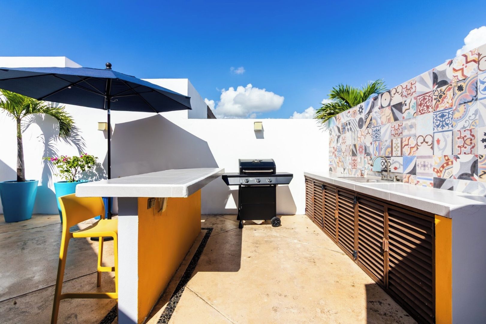An outdoor patio with a barbecue grill, a table with a chair, and a large umbrella.