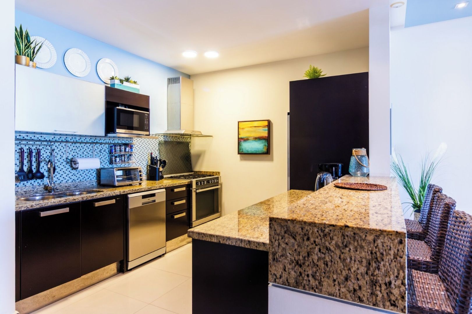 Een moderne keuken met granieten aanrechtbladen, roestvrijstalen apparatuur en een spatwand met een blauw-wit patroon.