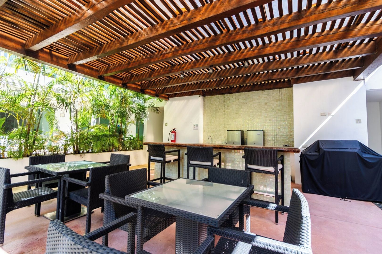 An outdoor patio with a wooden pergola, a bar area, and seating.