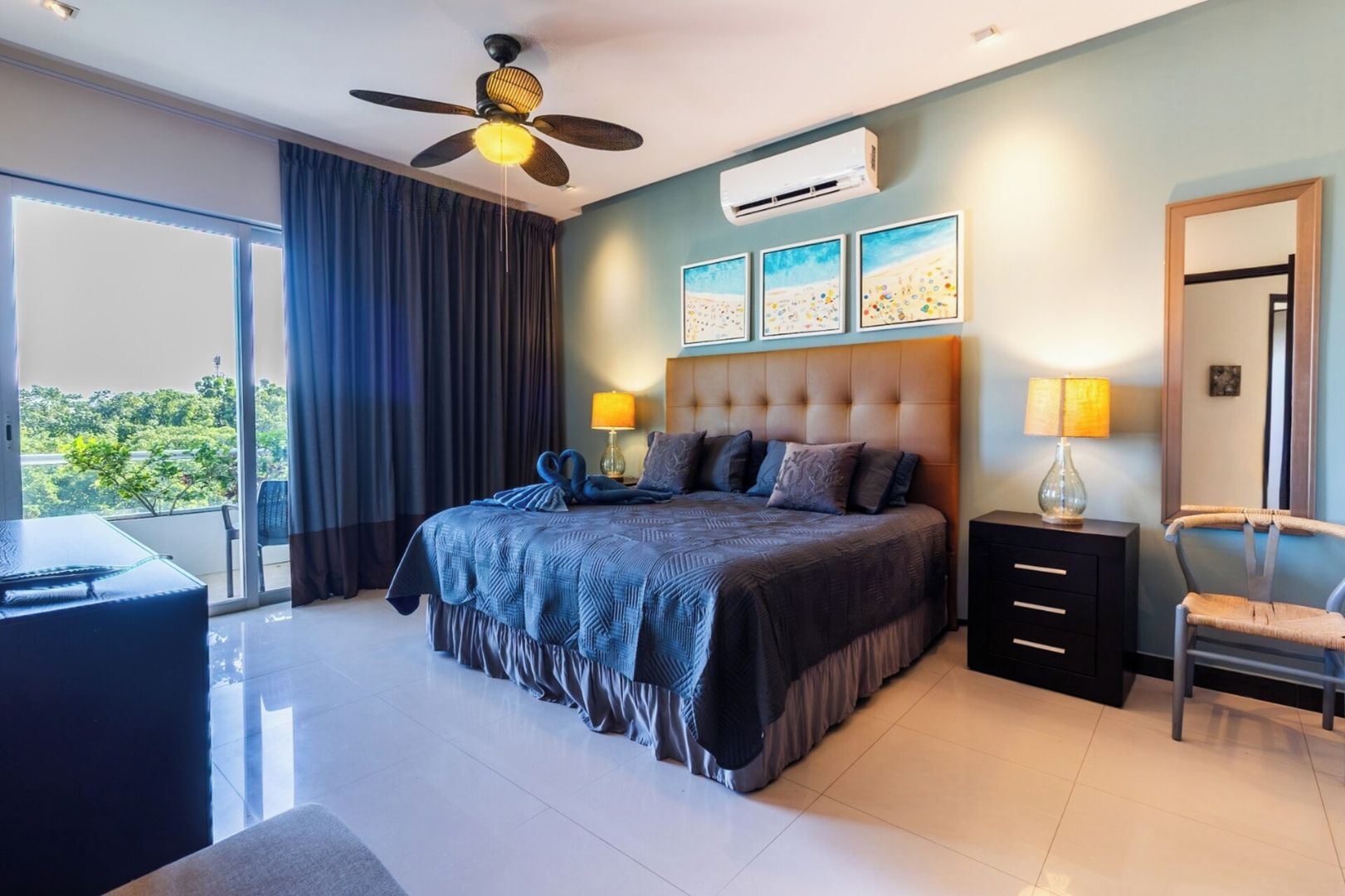 Ein modernes Schlafzimmer mit einem großen Bett, einem Deckenventilator, einer Klimaanlage und Blick auf Grün.