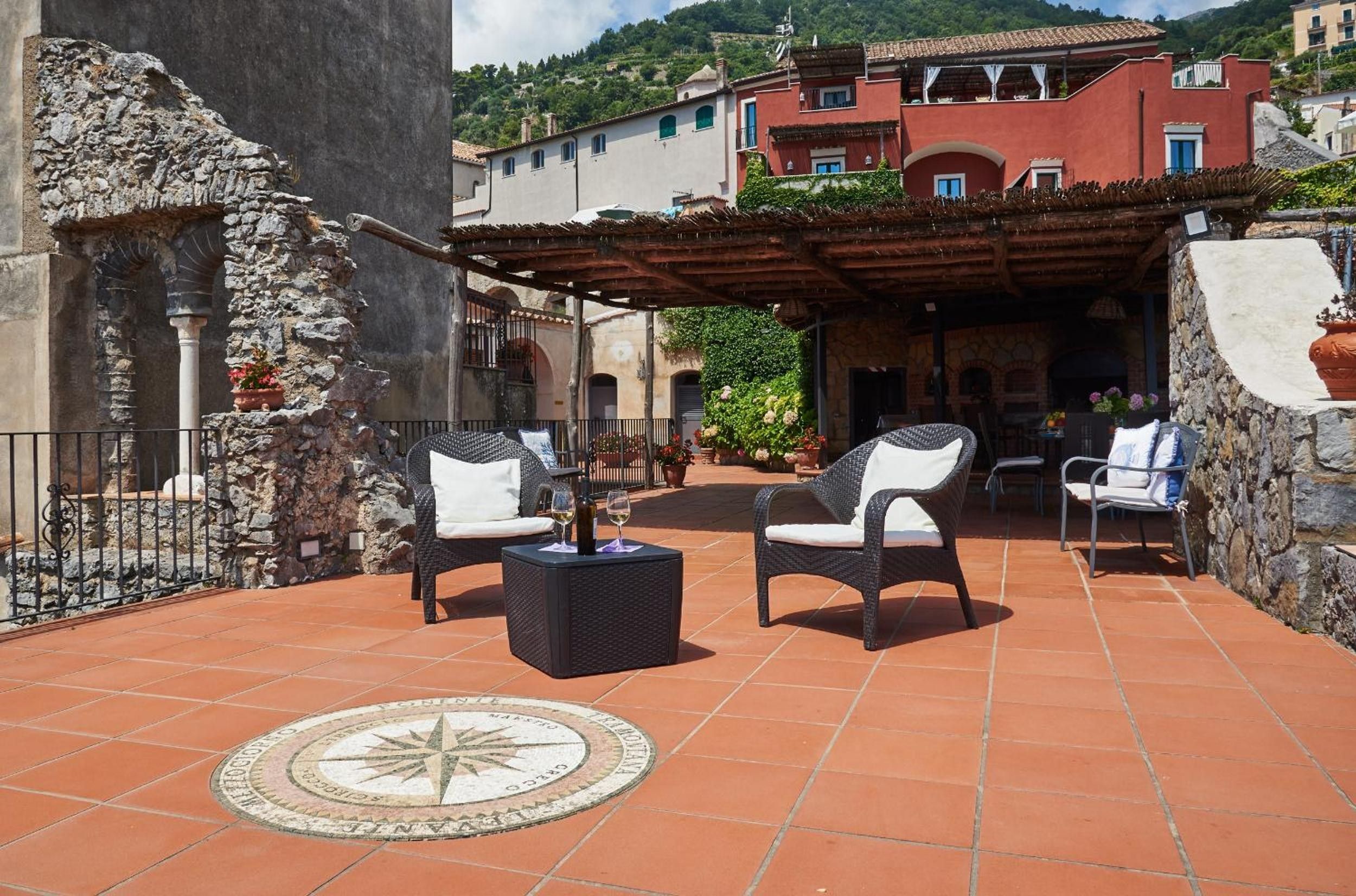 Une terrasse extérieure avec deux fauteuils en osier, une table et un motif de boussole dessiné sur le sol.