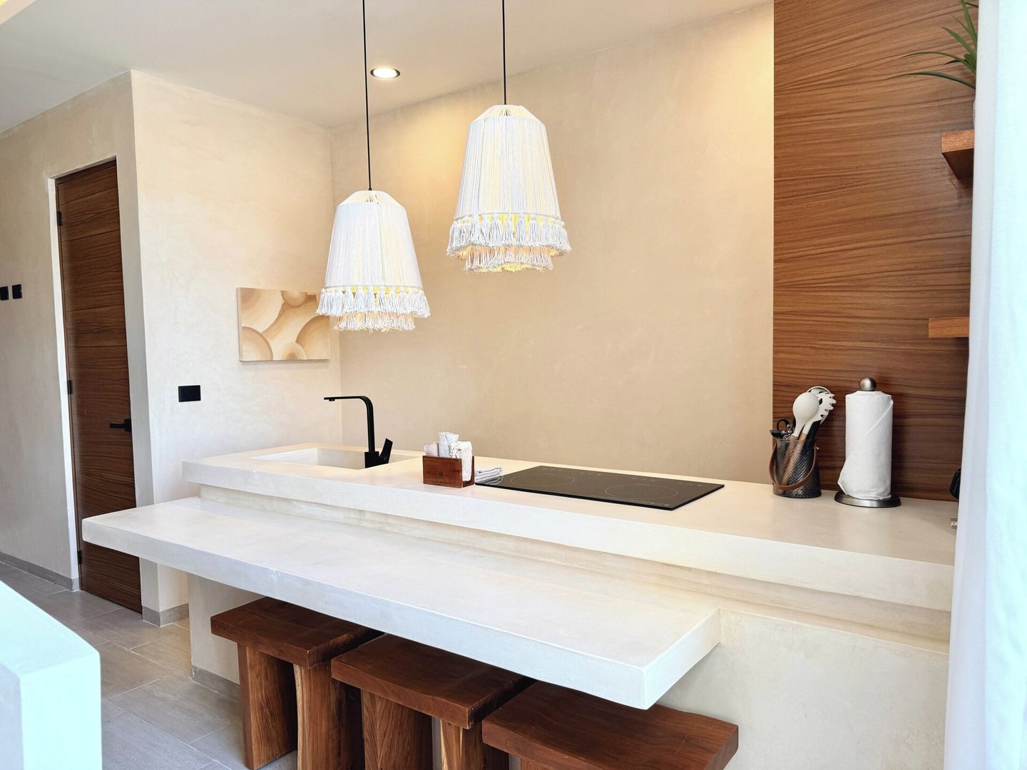 A modern kitchen with a white countertop, two pendant lights, a built-in stove, and wooden stools.