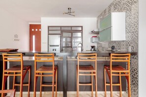 A kitchen with a central island, four wooden chairs, a refrigerator, a microwave, and a patterned backsplash. - Penthouse 3BR · Jacuzzi · 6 min a la playa (Playa del Carmen)