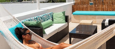 A hammock on a rooftop terrace with a sofa and a table.