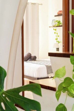 A bedroom with a bed, a curtain, a bedside table, a lamp, and a shelf with books and a plant. - Penthouse 3BR · Jacuzzi · 6 min a la playa (Playa del Carmen)