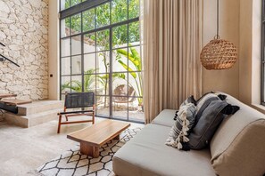 A modern living room with a stone wall, a sofa with cushions, a wooden coffee table, a wicker chair, and a hanging light fixture. - Townhouse with private pool facing the jungle (Tulum)
