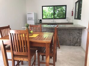 A compact kitchen with a built-in gas stove, a refrigerator, and a window with a view of greenery. - Sweet Apartment Tulum town and Great Pool (Tulum)