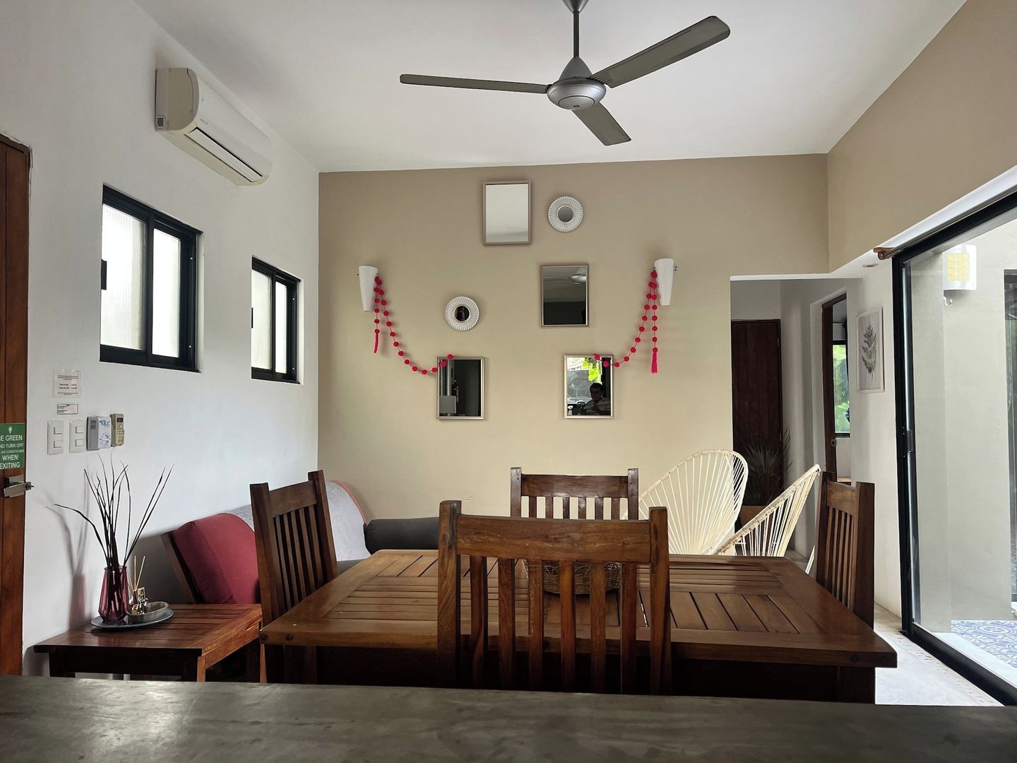 Un coin repas avec une table et des chaises en bois, un ventilateur de plafond et une vue à travers une porte vitrée.
