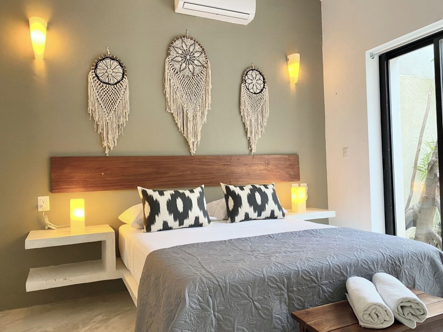 A bedroom with a bed, bedside tables, wall-mounted macramé wall hangings, and a window.