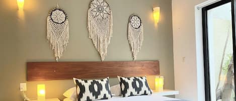 A bedroom with a bed, bedside tables, wall-mounted macramé wall hangings, and a window.