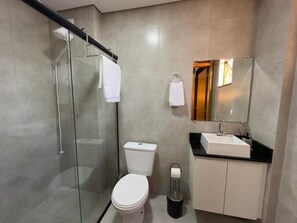 A modern bathroom with a glass shower enclosure, a toilet, a sink with a mirror above it, and a cabinet. - Aconchegante, moderno e completo URU 602 (Joinville)