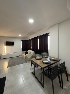 A modern living room with a dining area, a flat-screen TV mounted on the wall, a sofa, and a dining table set with plates and cutlery. - Aconchegante, moderno e completo URU 602 (Joinville)