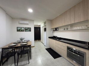 A modern kitchen with a dining area, featuring a black countertop, stainless steel appliances, and a black dining table with chairs. - Aconchegante, moderno e completo URU 602 (Joinville)