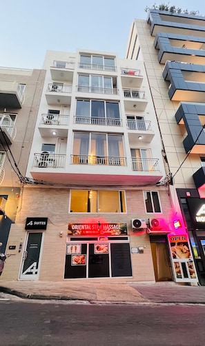 A multi-story building with a massage parlor on the ground floor, balconies on the upper floors, and a sign for '4 Suites' on the left. - St. Julian's Central Apartment 1 (St. Julian's)