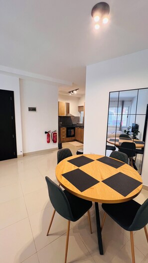 A modern dining area with a round table, black and wooden chairs, and a kitchen in the background. - St. Julian's Central Apartment 1 (St. Julian's)