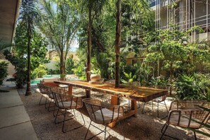 An outdoor dining area with a wooden table and wicker chairs, surrounded by lush greenery and a pool. - NUEVO Apartamento en La Veleta (Tulum)