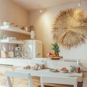 A modern kitchen with white appliances, a dining table set with plates and glasses, and a decorative wall hanging. - NUEVO Apartamento en La Veleta (Tulum)