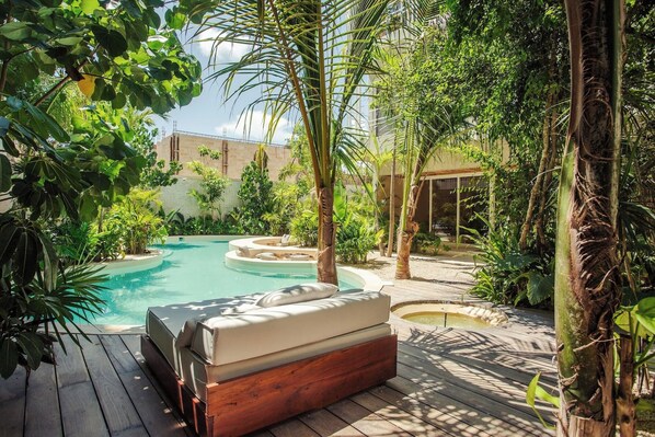 A pool area with a hot tub, surrounded by lush greenery and a wooden deck. - NUEVO Apartamento en La Veleta (Tulum)