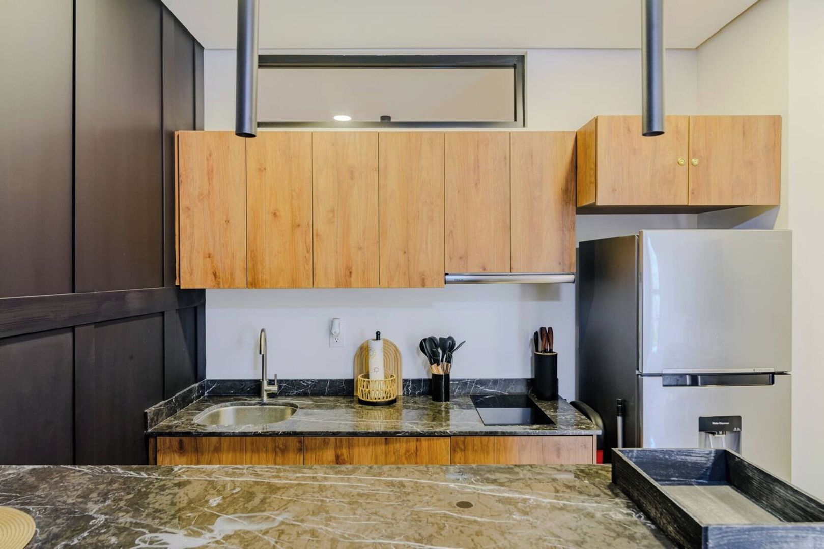 Une cuisine moderne avec des meubles en bois, un plan de travail en marbre, un évier et un réfrigérateur en acier inoxydable.