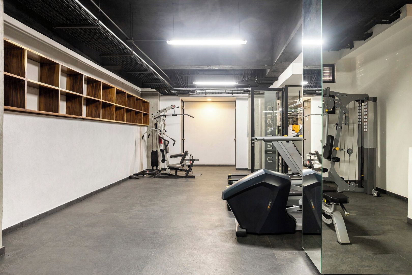 A gym with exercise equipment, a mirrored wall, and a wooden shelf unit.