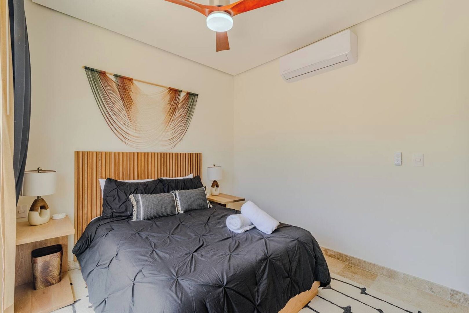 A hotel room with a bed, bedside tables, a ceiling fan, and a wall-mounted air conditioning unit.