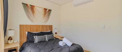 A hotel room with a bed, bedside tables, a ceiling fan, and a wall-mounted air conditioning unit.