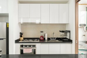 A modern kitchen with white cabinets, a stainless steel refrigerator, a gas stove, and a built-in oven. - Charm and comfort apartment in Aldea Zama (Tulum)