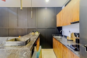 A modern kitchen with a marble countertop, wooden cabinets, and a built-in sink. - Charm and comfort apartment in Aldea Zama (Tulum)