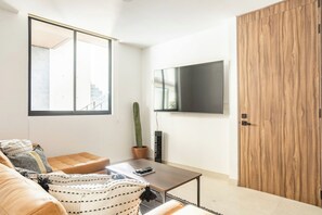 A modern living room with a sofa, a coffee table, a cactus plant, and a flat-screen TV mounted on the wall. - Charm and comfort apartment in Aldea Zama (Tulum)