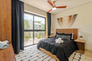A hotel room with a large bed, a ceiling fan, a view through the window, and a wooden headboard. - Charm and comfort apartment in Aldea Zama (Tulum)