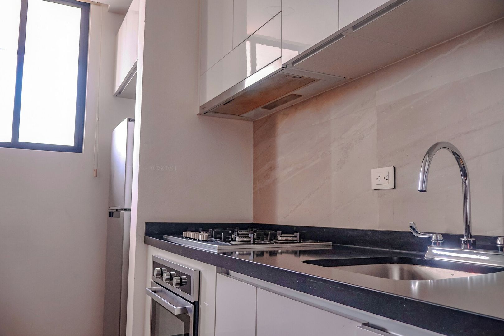 A modern kitchen with a stainless steel sink, a built-in oven, and a window providing natural light.