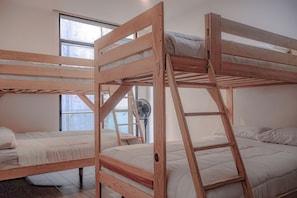 A room with three bunk beds made of wood, a standing fan, and large windows allowing natural light. - Relaxing Lakeside Retreat Pool Hot Tub and Patio (Tulum)