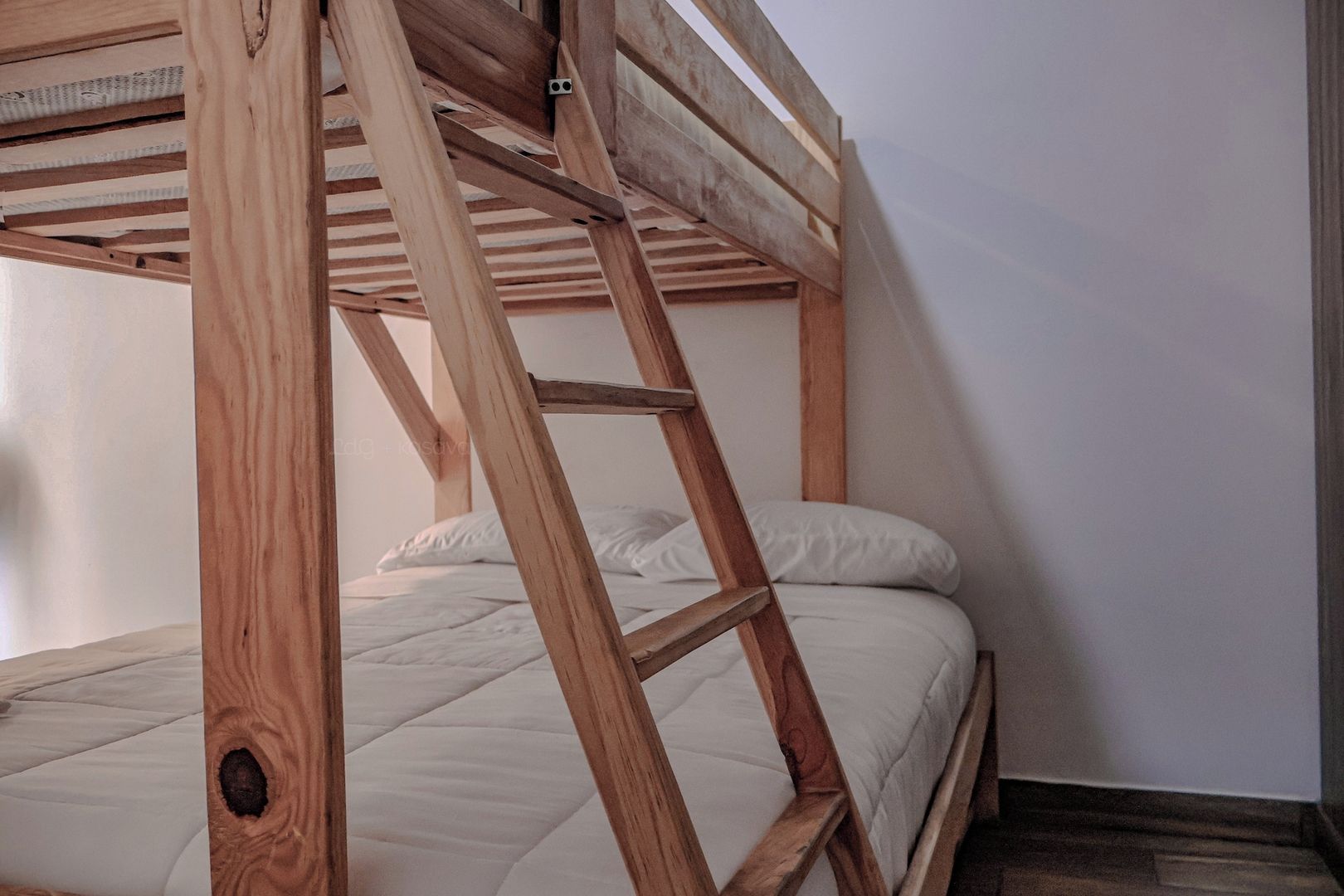A bunk bed with a wooden ladder, white bedding, and a plain wall.