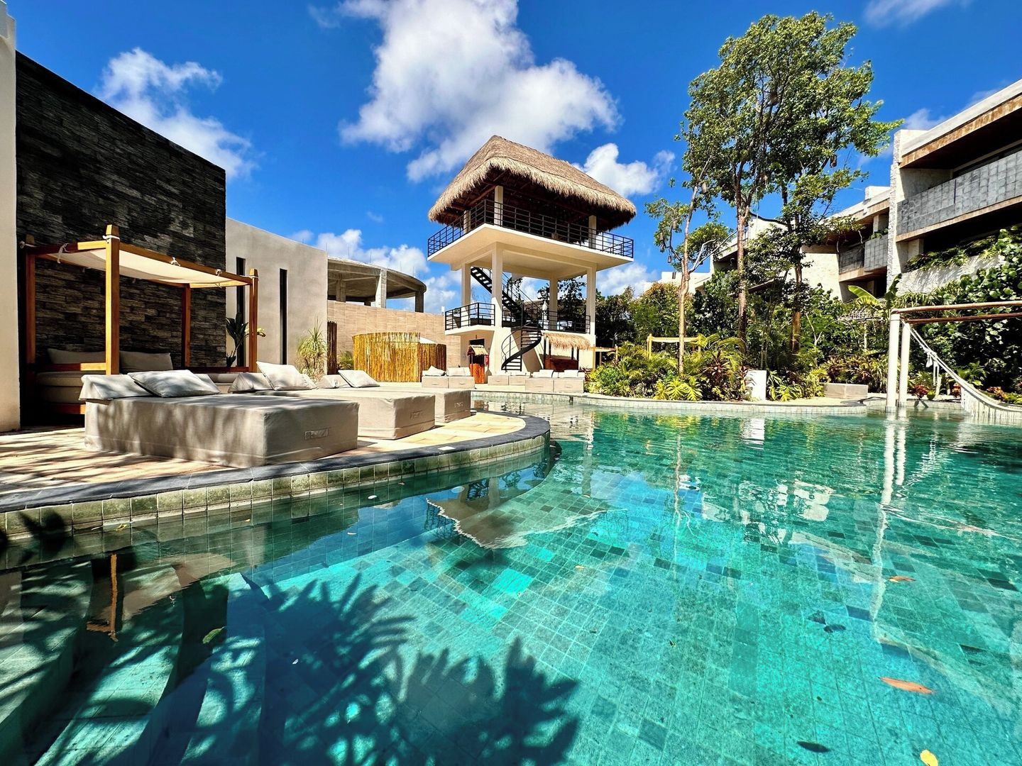 Una piscina con solárium y zona de descanso, rodeada de vegetación tropical.