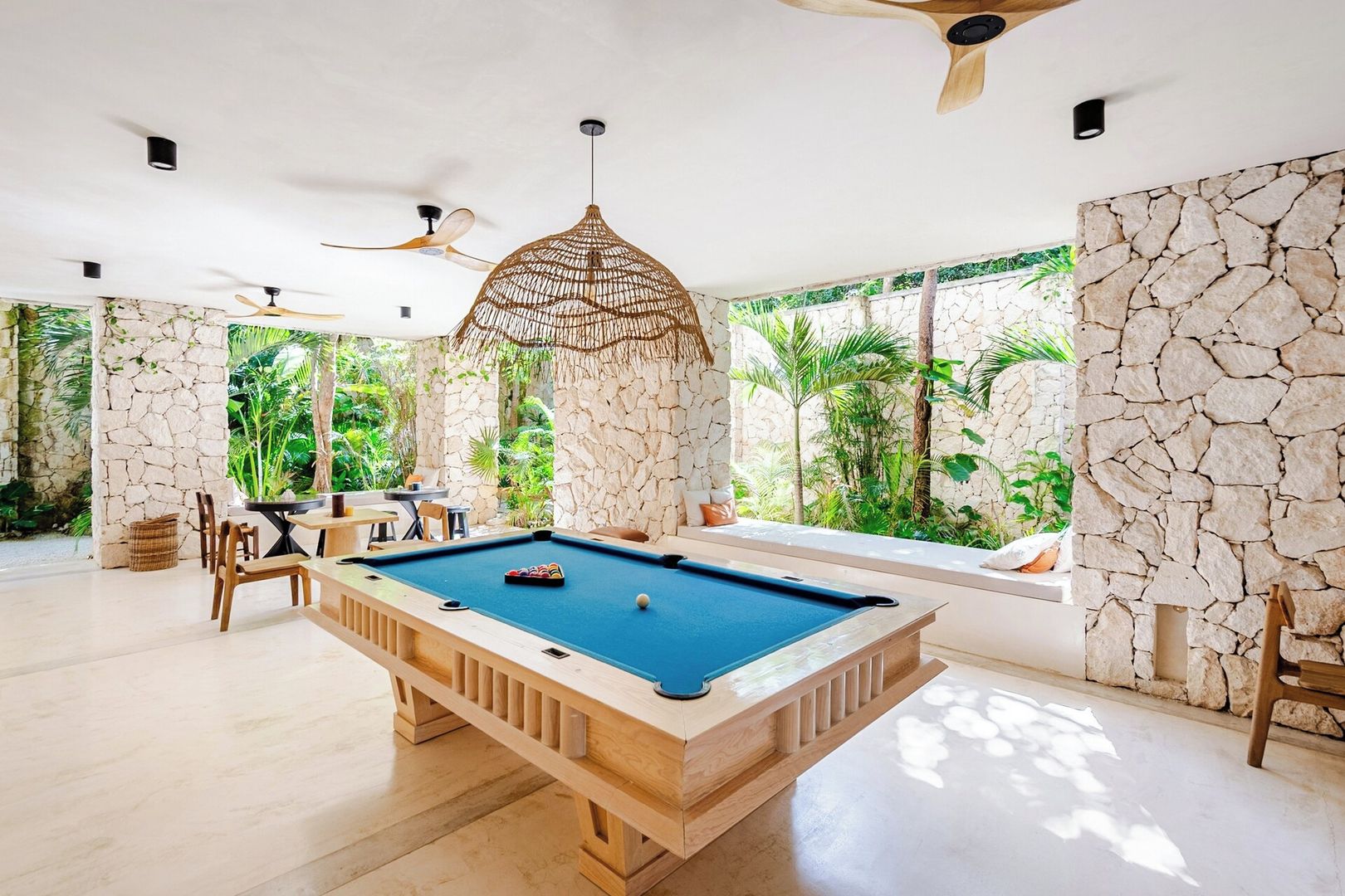 A pool table in a room with stone walls, ceiling fans, and a view of greenery.