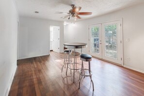 A room with hardwood flooring, a ceiling fan, a round table with bar stools, and a door leading to a balcony with glass doors. - Cozmo Hall on St Francis Ave (Columbus)
