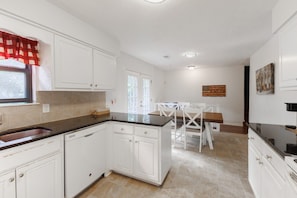 A kitchen with white cabinets, a black countertop, and a dining area with white chairs. - Cozmo Hall on St Francis Ave (Columbus)