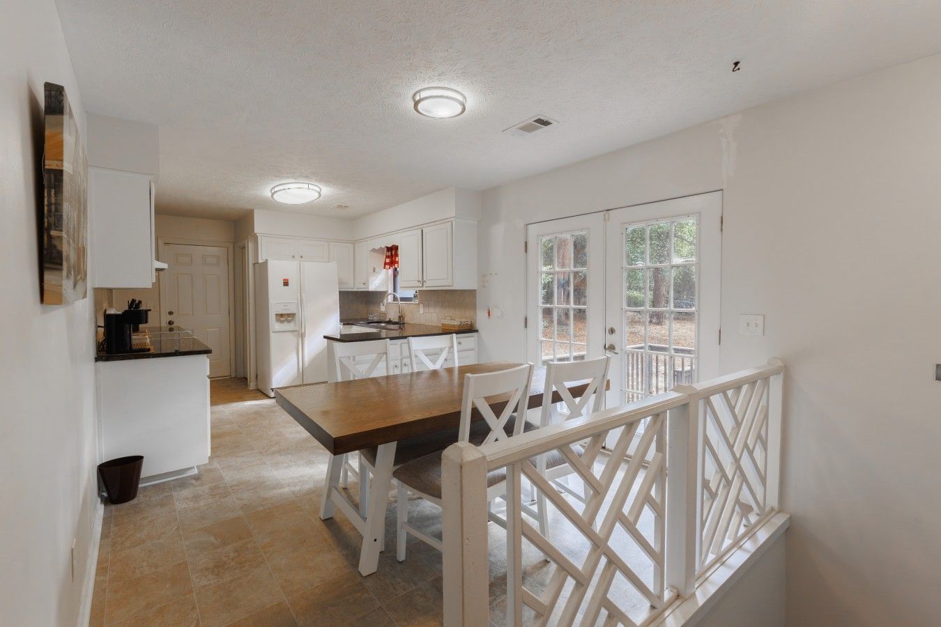 A spacious kitchen with white cabinetry, a wooden dining table, and a view through a glass door to an outdoor area.