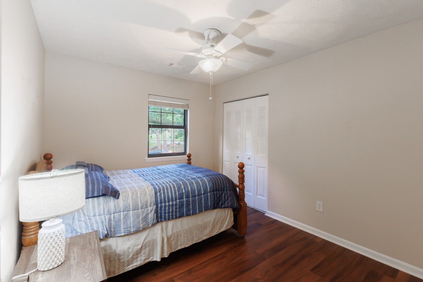 Une chambre à coucher avec un lit, une fenêtre, un ventilateur de plafond et une porte.